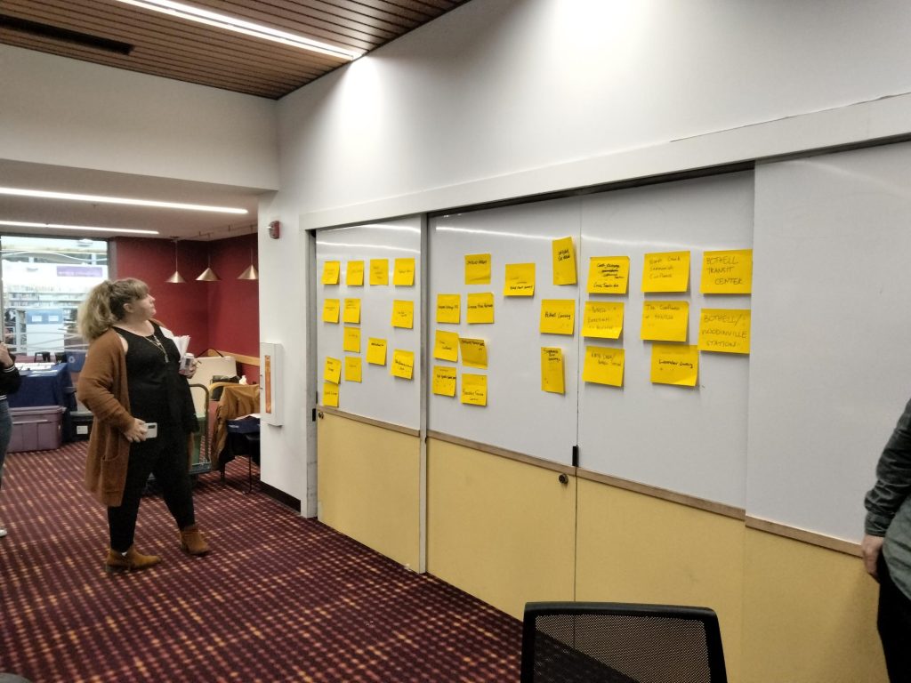 Woman looking at over 20 large yellow sticky notes on a whiteboard.