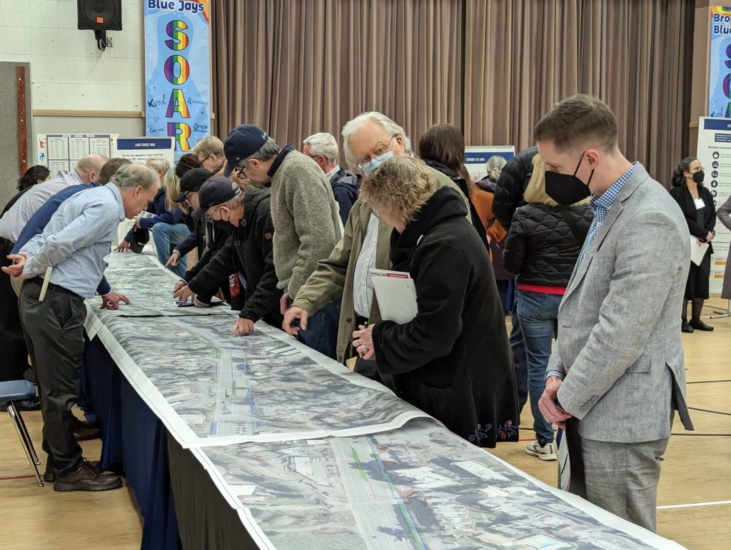 People standing next to tables and looking down at maps.