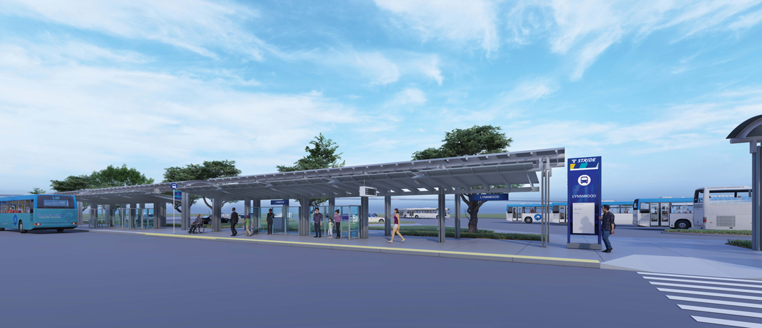 People sitting, standing, and walking under a covered bus shelter.